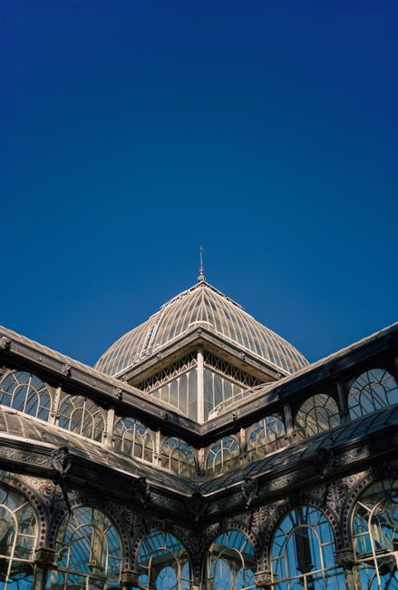 Photograph of the ornate glass and metal structure of Crystal Palace Park, showcasing its intricate architectural details with arched windows and a large domed roof, set against a clear blue sky. The image highlights well-maintained surfaces, clean glass panes, and polished metallic elements, emphasizing the importance of surface cleaning and maintenance for historic buildings. Cleaner Crystal Palace specializes in deep cleaning and sanitisation of such surfaces to preserve architectural beauty, with visible reflections and bright, dust-free surfaces indicative of professional cleaning efforts.